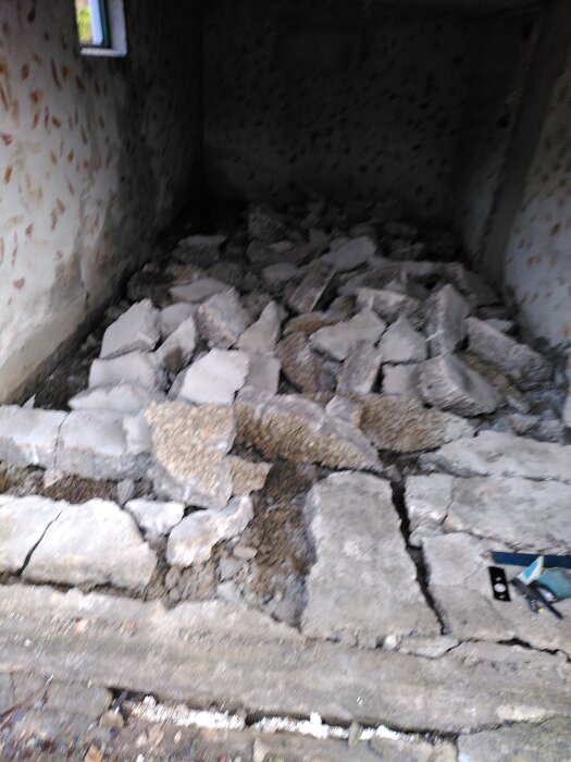 Krossad betong på golvet i ett gammalt garage under rivning, med verktyg synliga i hörnet. Betongdelarna är ojämnt spridda över ytan.