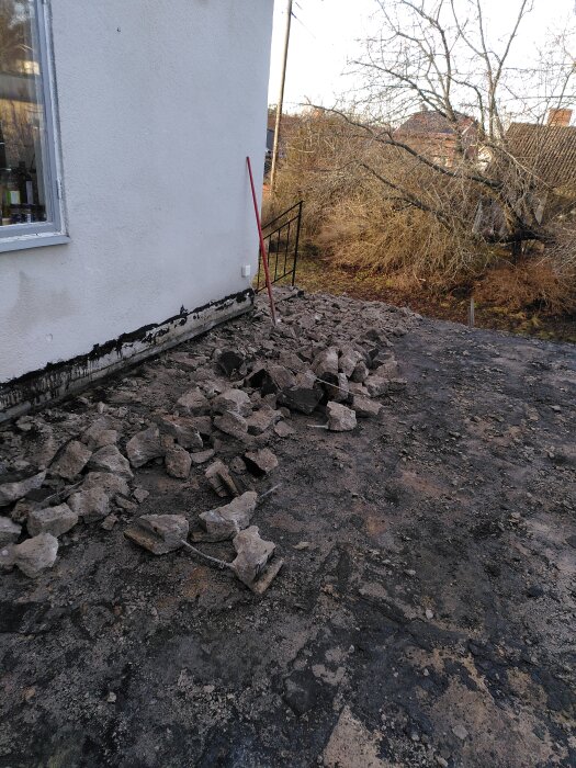 Betongrester vid sidan av ett hus där garagegolvet bilats upp. En röd spade står lutad mot husväggen. Bakom syns träd och buskage.