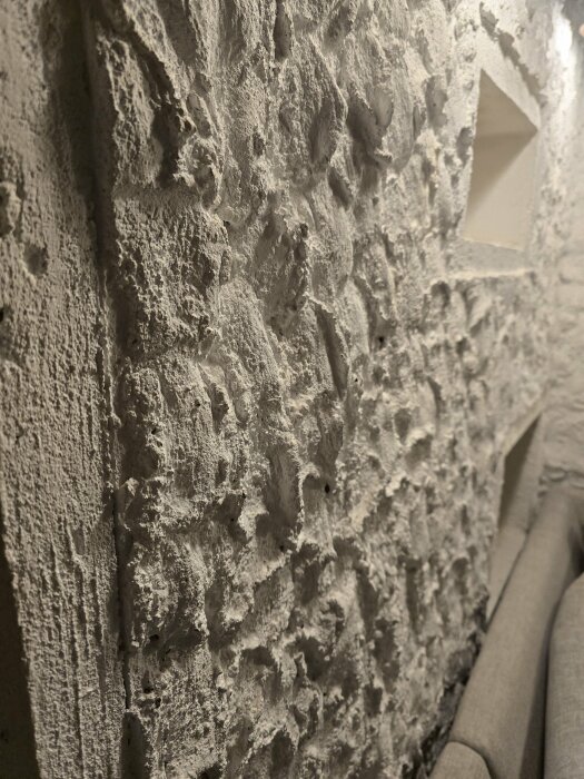 Närbild på en inomhusvägg med kraftig putsad struktur i ett gårdshus, möjligtvis utfört med lekablock och målad yta.