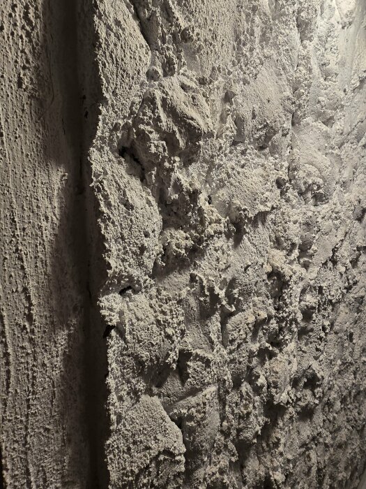 Kraftigt strukturerad puts på innervägg i gårdshus, med ojämn yta och grov textur.