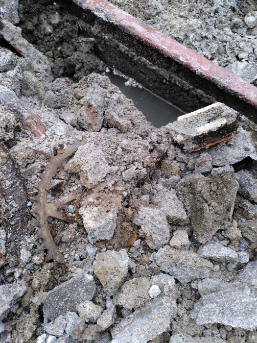 Betonghög med skrot och rostiga cykeldelar synliga bland stenar och murbruk, en del av en byggarbetsplats under renovering.