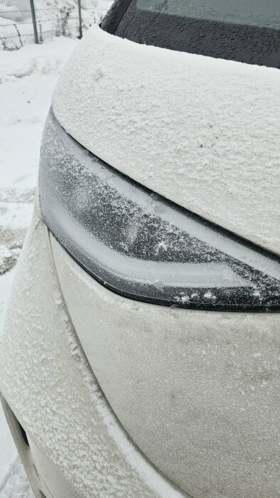 Bilens strålkastare täckt av frost och snö i minusgrader, visar behovet av uppvärmda strålkastare för bättre körförhållanden i kallt väder.