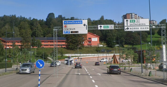 Vägskyltar mot Härnösand med riktningar för E4 mot Skönsberg och Norra Kajen, omgivna av fordon och byggnader i bakgrunden.