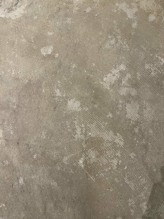 Betonggolv i källare med rester av lim efter borttagen plastmatta; ytan ser fläckig och ojämn ut.