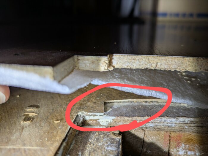 Närbild av golvkonstruktion med linoleum inringat, som ligger på två lager masonitskivor, vilket syns i nivåskillnaden mot råsponten.