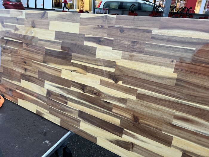 Träskiva med varierande mörka och ljusa trätoner, troligtvis en bordsskiva, ligger på ett bord i en butiksmiljö.