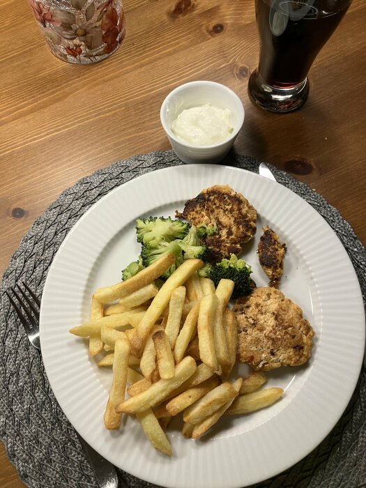 Tallrik med laxburgare, pommes frites och broccoli, tillsammans med en skål grekisk yoghurt och ett glas dryck.