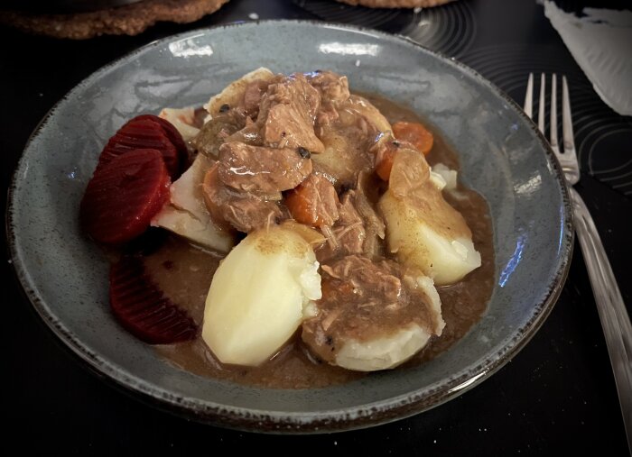 Kalops med kokt potatis och inlagda rödbetor på en tallrik.