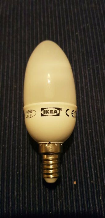 Vit lampa från IKEA med skruvsockel, placerad på en mörk yta.