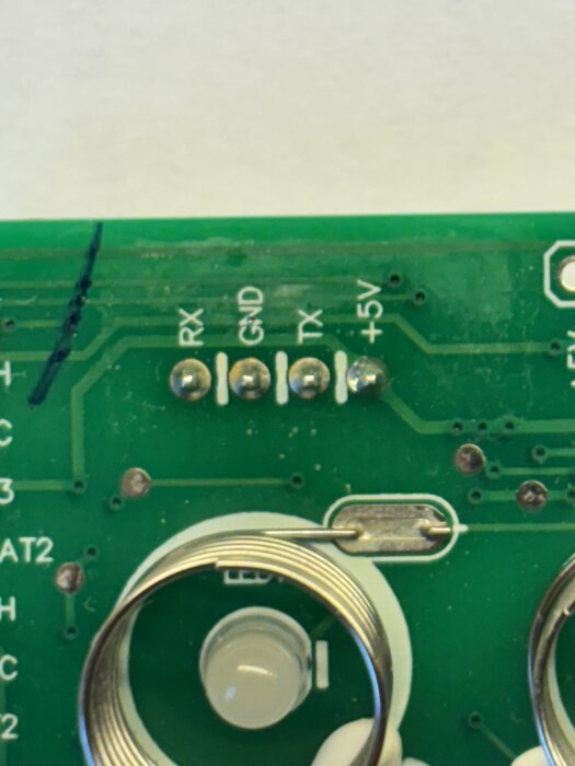 Närbild av ett kretskort med markerade anslutningar: RX, GND, TX, +5V, samt delar av en termistor synlig nedanför.