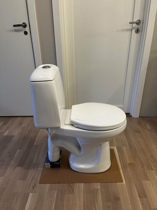 Wostman Ecoflush toalett med cistern och sits på träunderlag i rum med stängd dörr, pappershandduk under som torkar upp vatten.