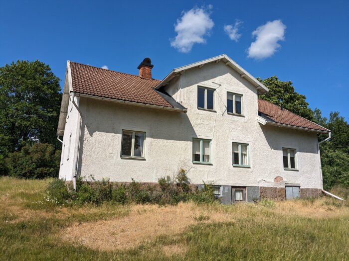 Boningshus på landsbygden i Eksjö med tegeltak och vit fasad, omgivet av gräs och träd under en blå himmel.