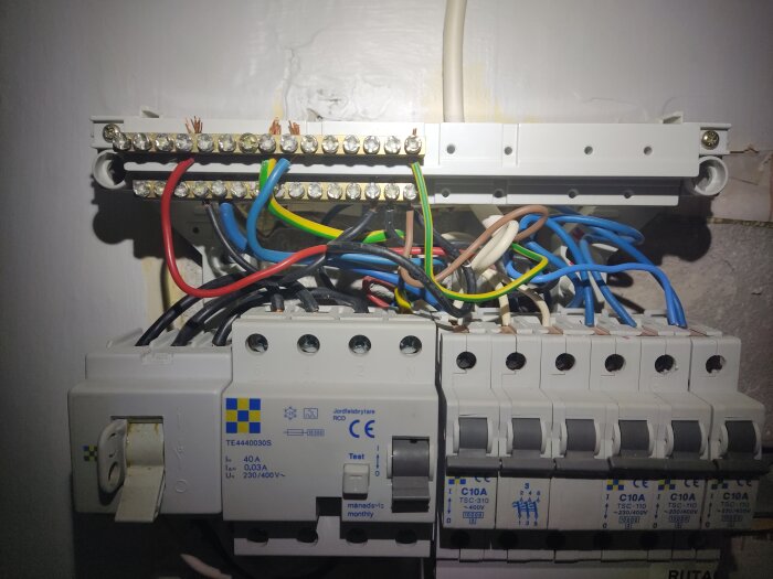 Elcentral med olika kablar i en lägenhet, inklusive en röd kabel som nämns i texten. Kablarna är anslutna till jordfelsbrytare och säkringar.