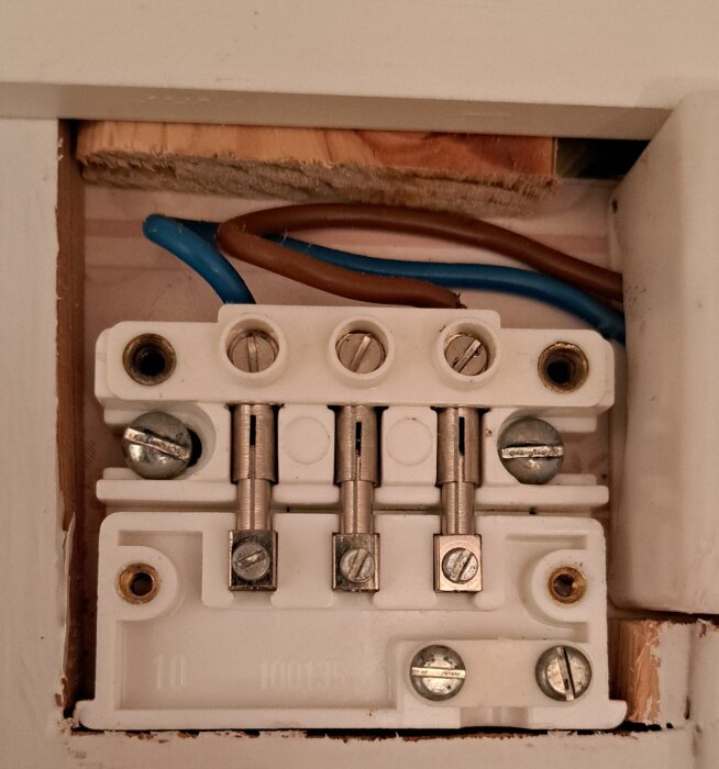 Närbild på en vit elektrisk anslutningsplint med flera kablar kopplade till den inuti en vägginstallation.
