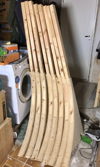 Träväggar böjda i bågar står lutade mot en vit dörr nära en tvättmaskin i ett hemmagarage.