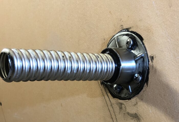 Metallisk spiralfjäder genom en väggmonterad fläns.