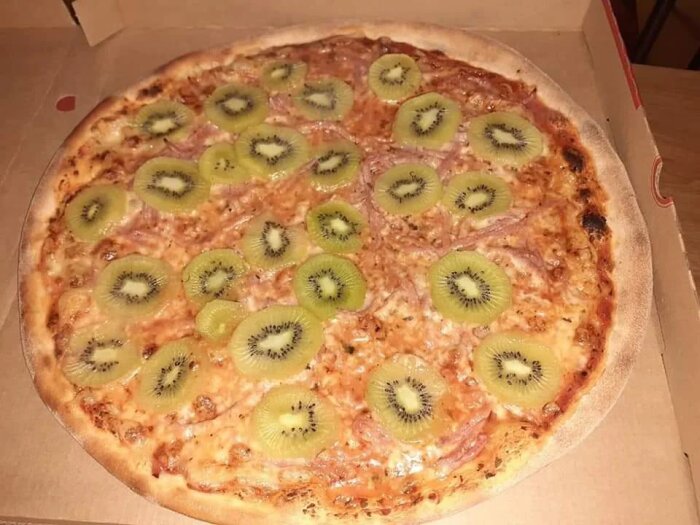 Pizza täckt med skivor av kiwi i en öppen kartong.