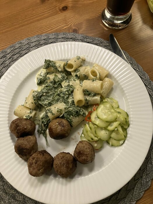 Köttbullar med rigatoni och grönkål i ädelostsås, ingefärsgurka och ett glas must på ett träbord.