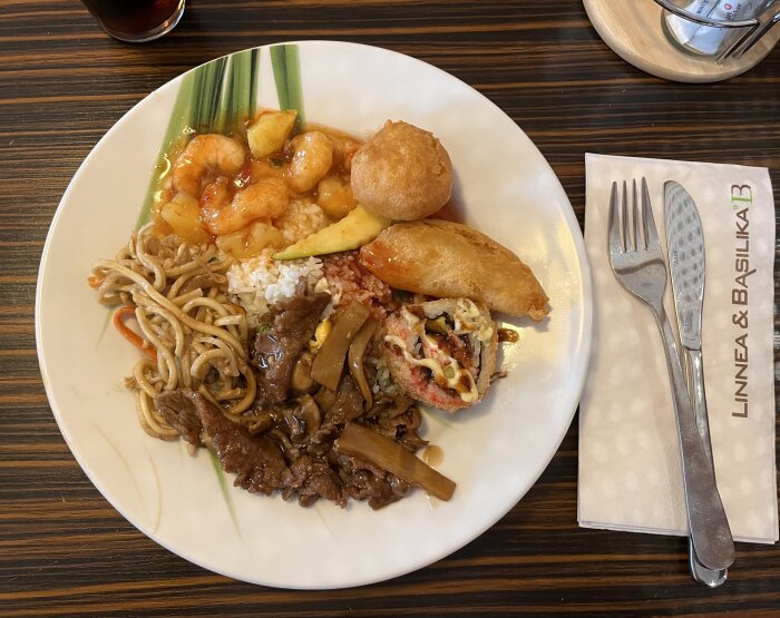 En tallrik med en blandning av asiatiska rätter inklusive nudlar, biff, ris, räkor, vårrulle och sushi.
