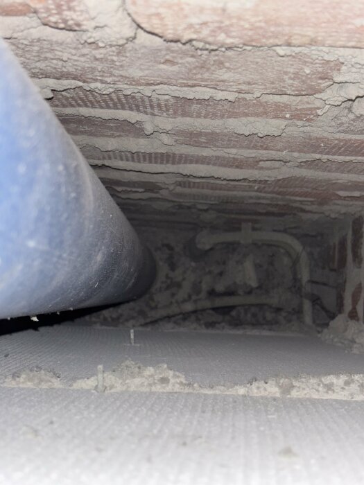 Gulmarkerat område bakom en lucka med rör och tegelvägg; potentiell ventilation eller skvallerrör för inkommande vatten.