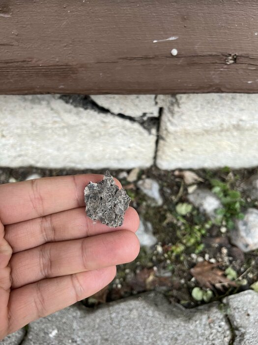 Spricka i husgrund från 60-talet, bit av trasigt material hålls upp framför skadan.