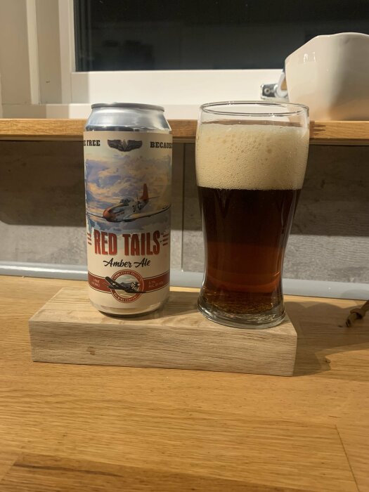 En ölburk märkt "Red Tails Amber Ale" står bredvid ett glas fyllt med mörk öl, placerat på en träplatta.