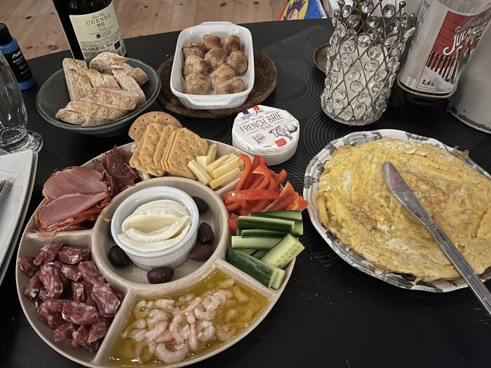 Upplagd plockmat med chark, ost, räkor och grönsaker, serverad med omelett och nybakat surdegsbröd samt vinflaska i bakgrunden.