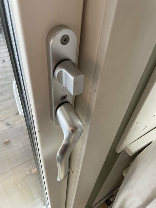 Handtag och lås på altandörrens insida, med silverfärgad finish, delvis insyn till altanen.