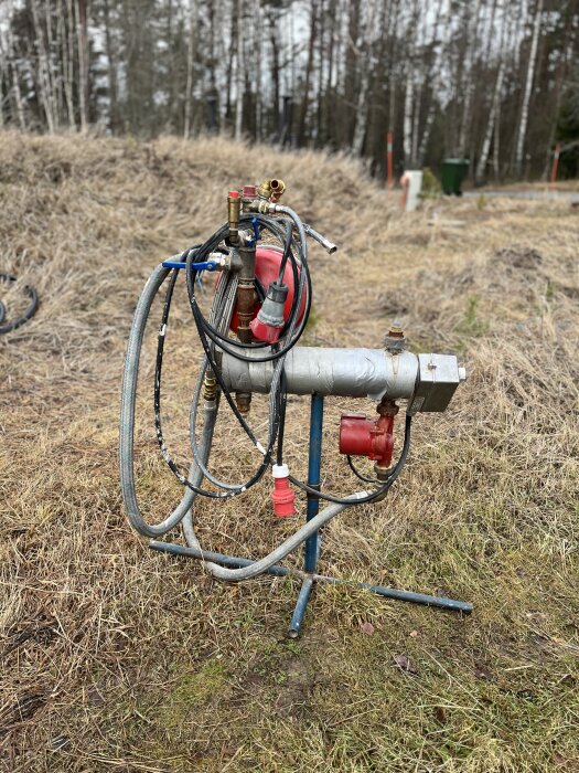 En byggpanna på ett stativ utomhus med rör och slangar i en skogsmiljö.