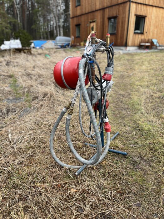 Byggpanna 9kW med slangar och manometer stående på torrt gräs framför ett trähus.