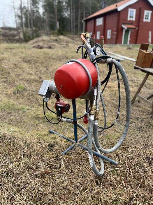 Röd byggpanna 9kW med slangar och ventiler utomhus, i bakgrunden ett rött hus. Används för värme och torkning av betong.