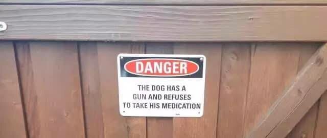 Skylt på ett trästaket med texten "Danger: The dog has a gun and refuses to take his medication".