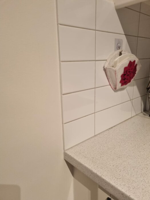 Kök med ljus laminatbänkskiva, vit kakelvägg och en röd dekoration på väggen. Avstånd mellan bänkskivan och kaklet syns.