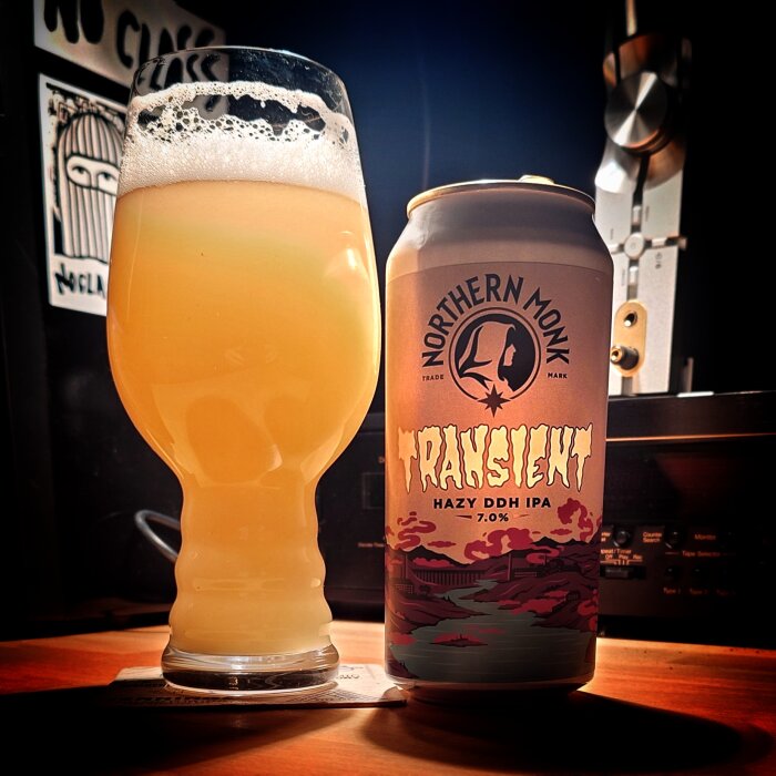 En glas med disig IPA bredvid en burk Northern Monk Transient Hazy DDH IPA, 7.0%, på ett bord.