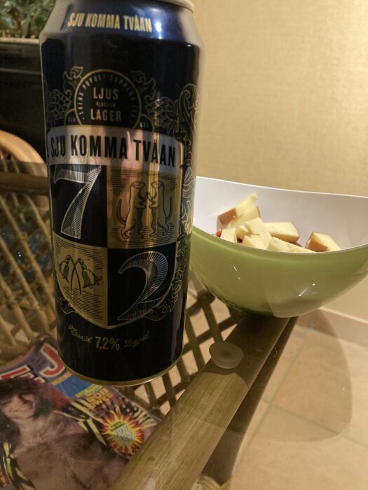 En ölburk märkt "Sju Komma Tvåan" bredvid en skål med ostbitar på ett glasbord.