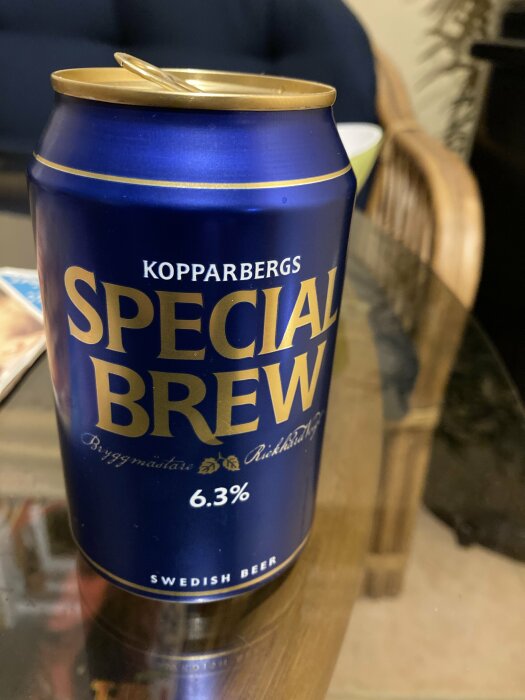 En burk Kopparbergs Special Brew 6,3% öl står på ett bord, omgiven av en del av en stol och annan inredning.