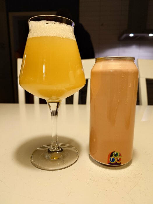 Ett glas fyllt med ljus, grumlig dryck bredvid en oöppnad burk öl på ett bord.