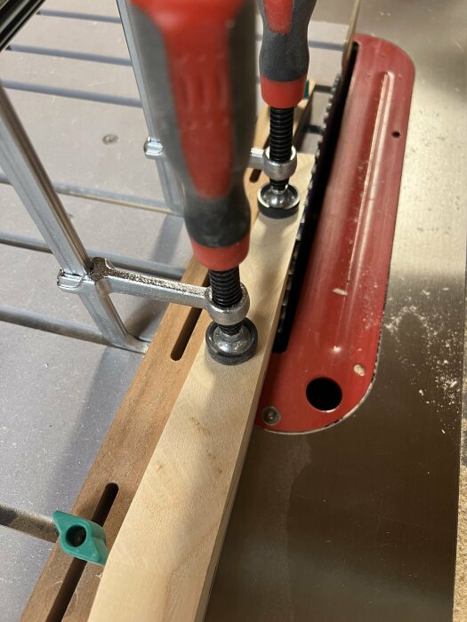 Två kinesiska tvingar håller fast en träbit på en bordsåg med rött inslag.