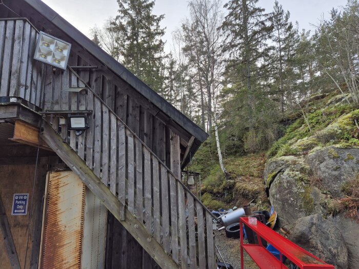 Trägarage med 41 graders takvinkel vid skogskant, rostig dörr och skylt som säger "Parking Only". Röd ställning i förgrunden.