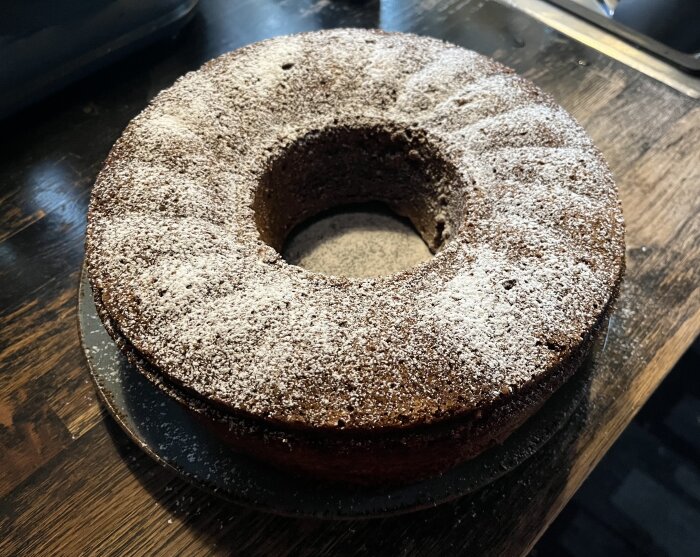 Fluffig banankaka med florsocker på toppen, bakad med mogna bananer och malen kardemumma, på en mörk bänkskiva.