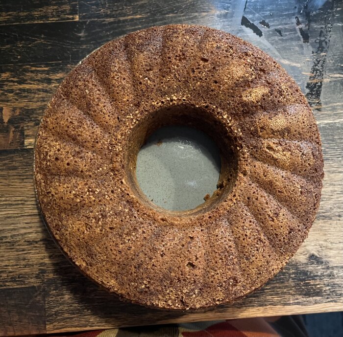 Banankaka med gyllenbrun yta, bakad i en form med mönster, placerad på ett rustikt träbord.