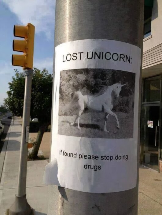 Affisch på lyktstolpe med bild av enhörning och texten "Lost Unicorn: If found please stop doing drugs", bredvid trafikljus.