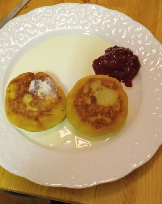 Två småländska kroppkakor med brun stekyta på en tallrik, serverade med lingonsylt.
