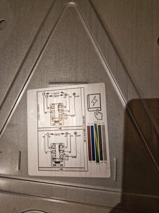 Instruktionsdiagram på metallisk yta visar elektriska anslutningar och ledningskonfiguration för kökshällinstallation.
