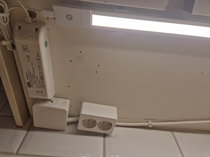Jordad elinstallation under köksskåp med dubbeluttag och LED-kökslampa. Kopplingslådan är lite snedjusterad.