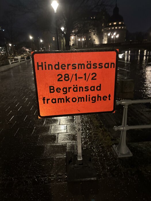 Skylt vid nattlig gata som meddelar "Hindersmässan 28/1–1/2 Begränsad framkomlighet" i orange och svart text, upplyst av gatubelysning.