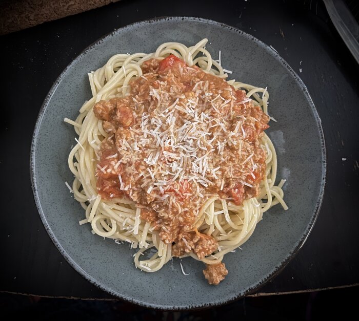 Tallrik med pasta toppad med köttfärssås och riven parmesan.
