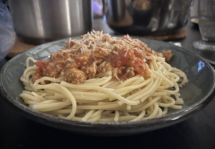 Tallrik med spaghetti och köttfärssås toppad med riven parmesanost.