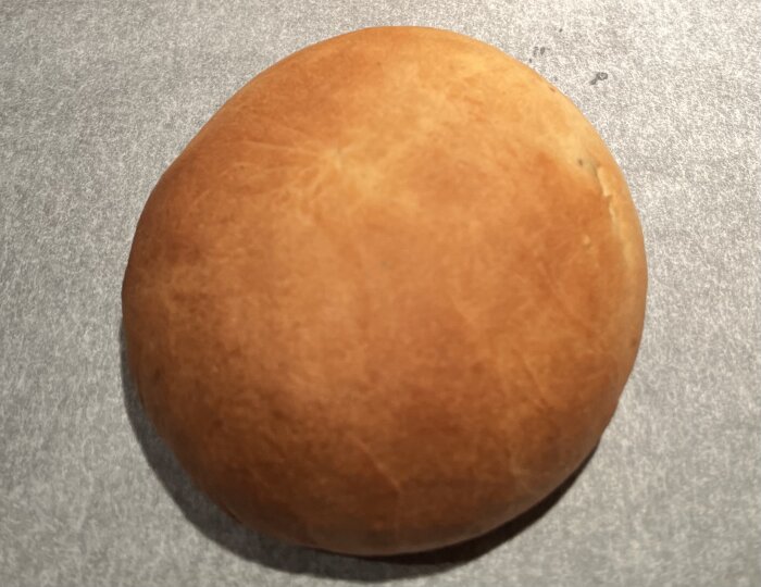 Nygräddad semmelbulle utan florsocker på ett bakplåtspapper.