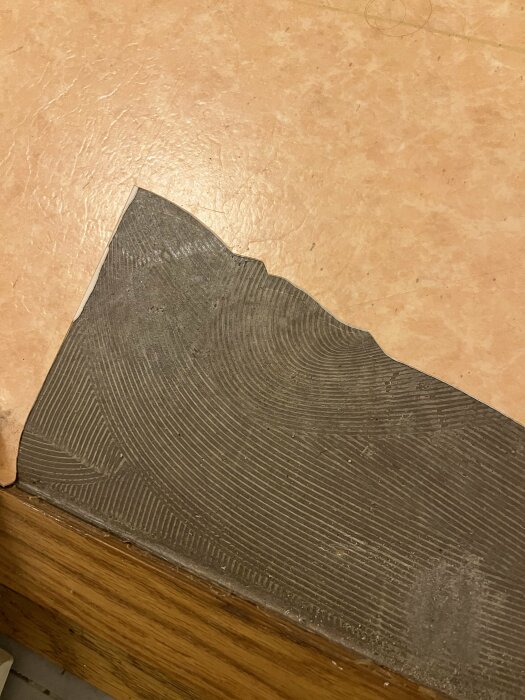 Skadad del av ett golv där en bit av mattan saknas, exponerar underlagets struktur och olika materiallager.